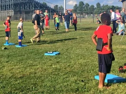 A young athlete completes a C3 balance assessment on a field with a tablet secured behind their back.